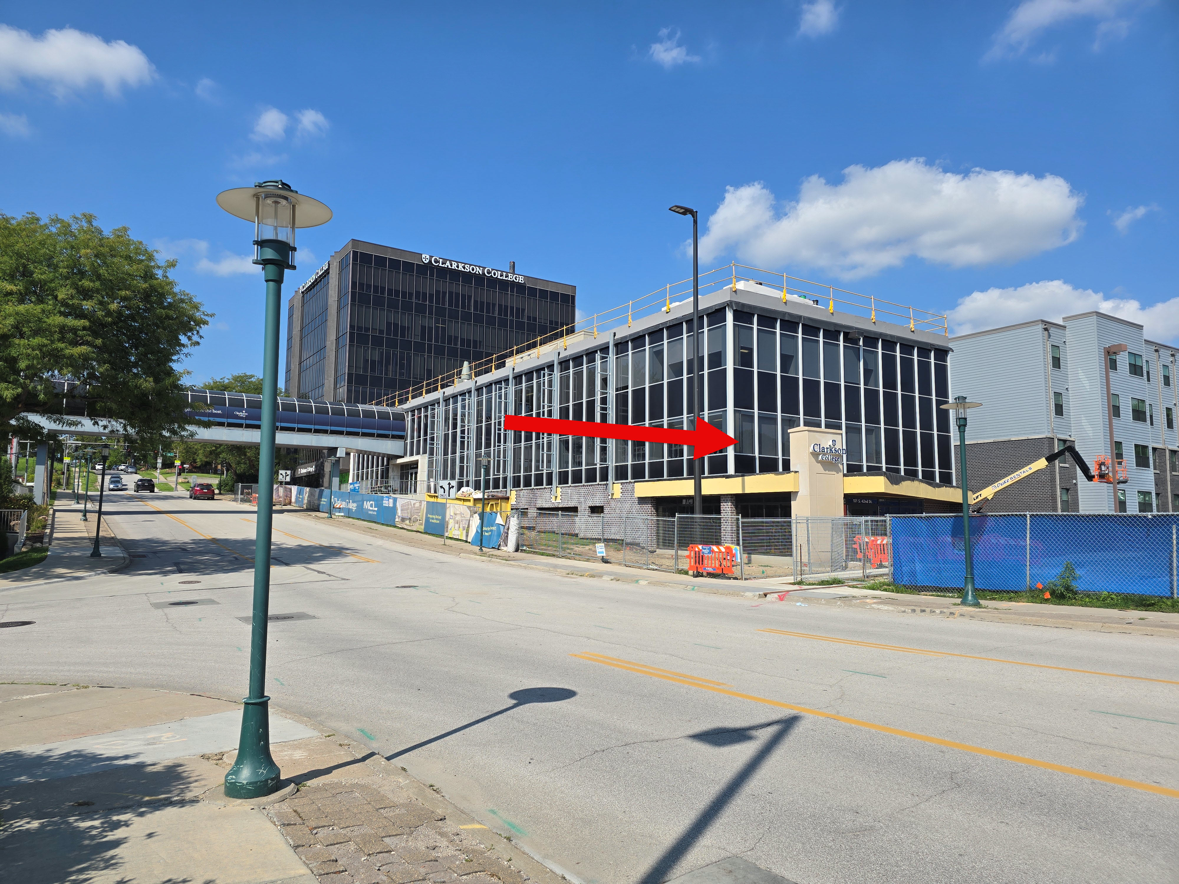 a picture of the new entrance with a red arrow pointing to the area between the fences where the door is located.